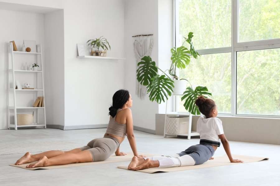 Une femme et une enfant pratiquent le cobra dans un salon lumineux pour évacuer le yoga et stress quotidien.