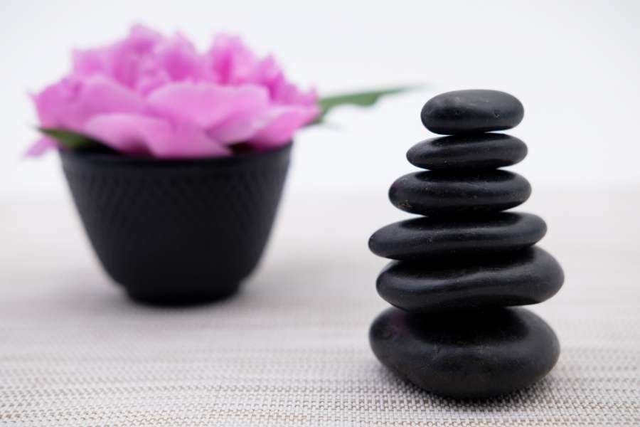 Piles de galets noirs lisses disposés en équilibre à côté d'un bol contenant une fleur rose pour le massage aux pierres chaudes.