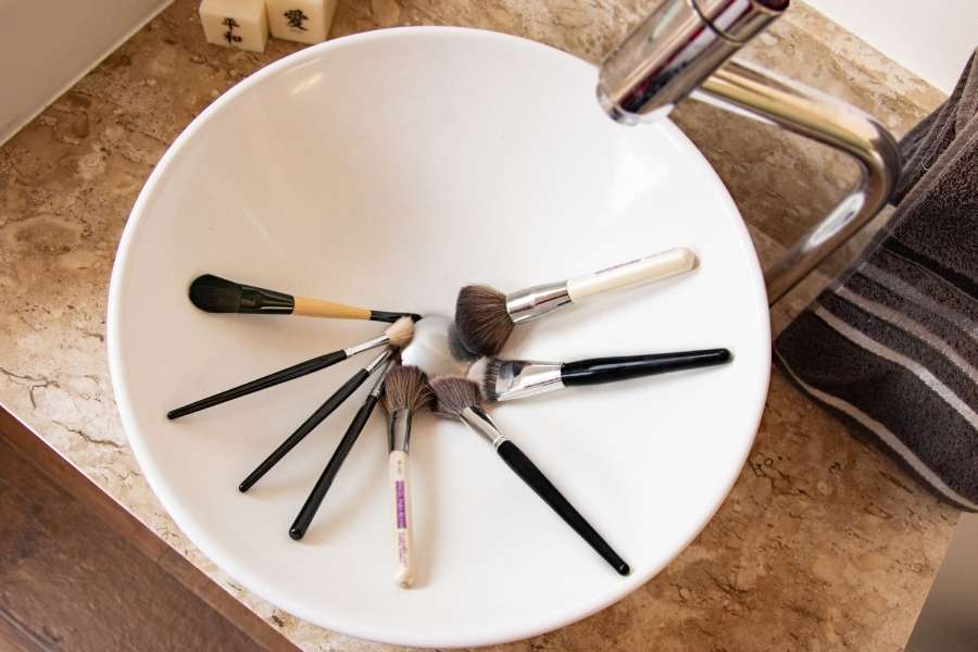 Plusieurs pinceaux de maquillage disposés au fond d'une vasque blanche avant de nettoyer ses pinceaux de maquillage.