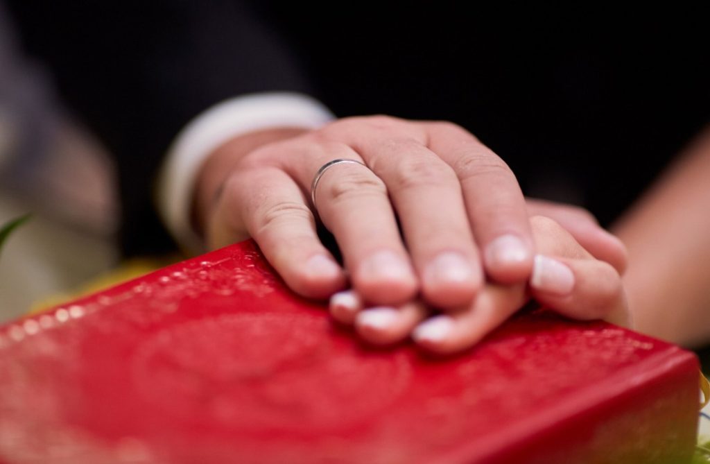 Mains des mariés avec alliance posées sur la Bible durant les etapes et traditions mariage religieux.