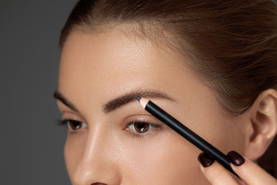 Une main utilise un crayon de maquillage pour tracer et redessiner avec précision la ligne d'un sourcil.